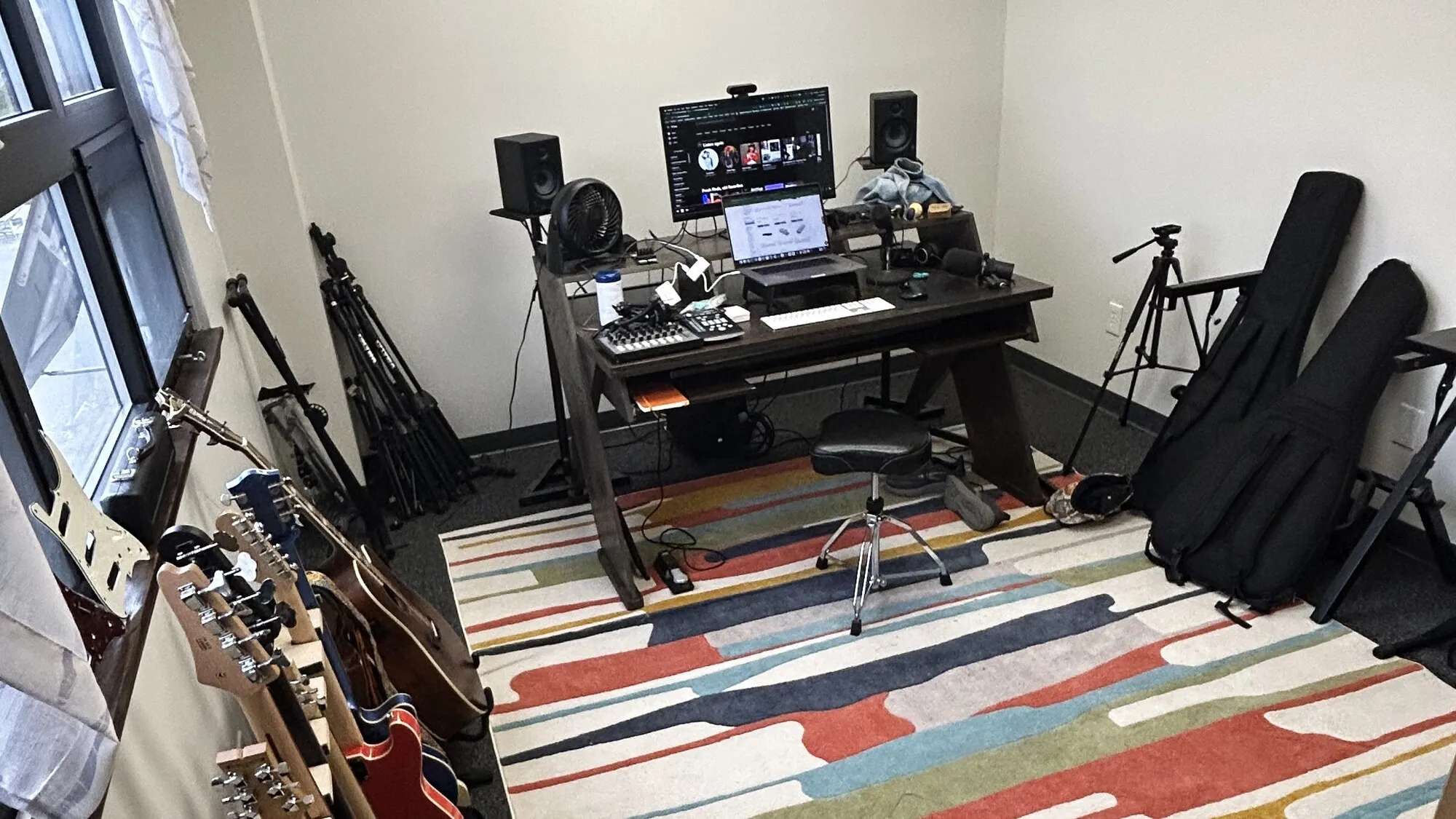 The studio: a wall rack of guitars, a desk with studio monitors, an audio interface and a keyboard, and open floor space to work in.